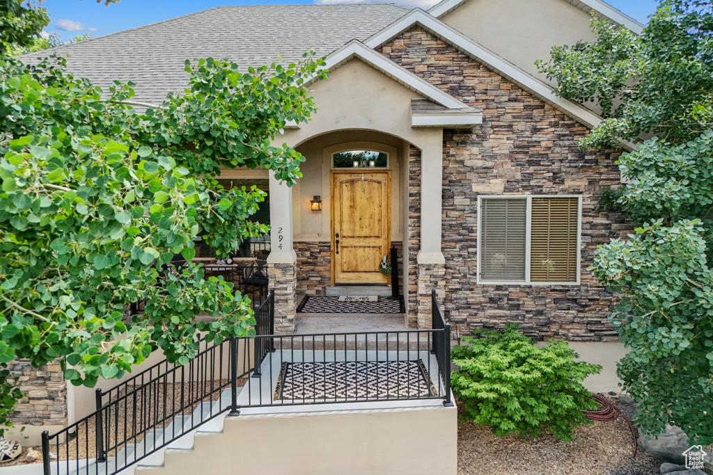 Property entrance with stone siding, stucco siding, and a shingled roof