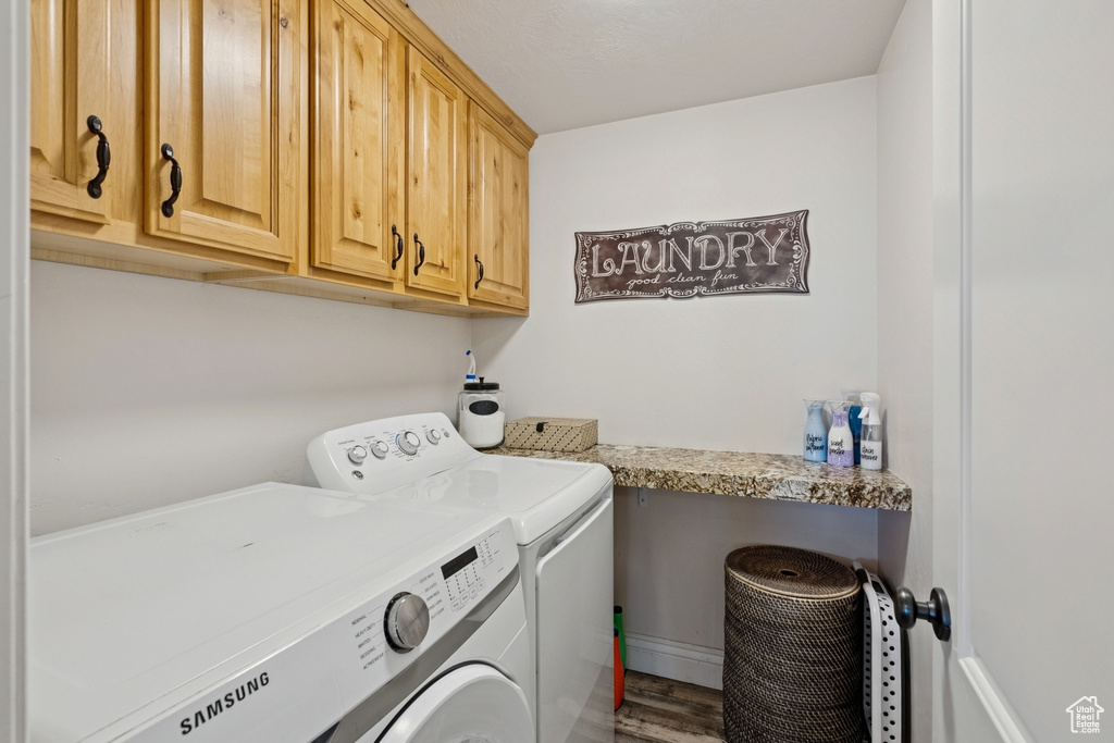 Laundry area with washing machine and clothes dryer, cabinet space, and wood finished floors