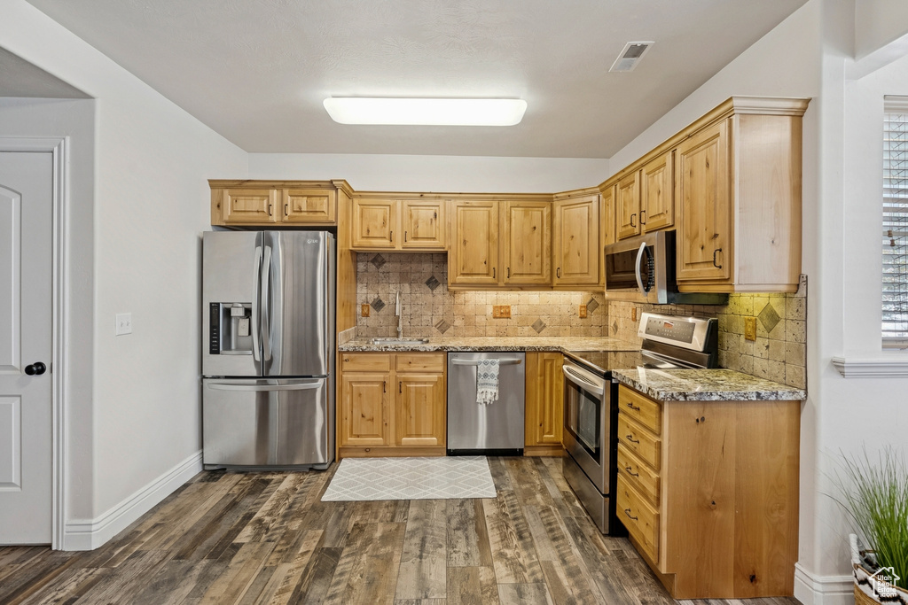Kitchen with stainless steel appliances, dark wood-style floors, light stone countertops, and backsplash