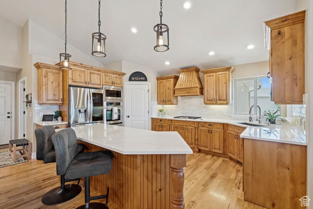 Kitchen featuring stainless steel appliances, premium range hood, a center island, tasteful backsplash, and light wood finished floors