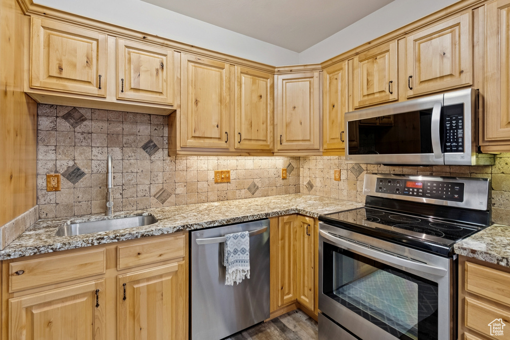 Kitchen with appliances with stainless steel finishes, tasteful backsplash, light brown cabinets, and light stone countertops