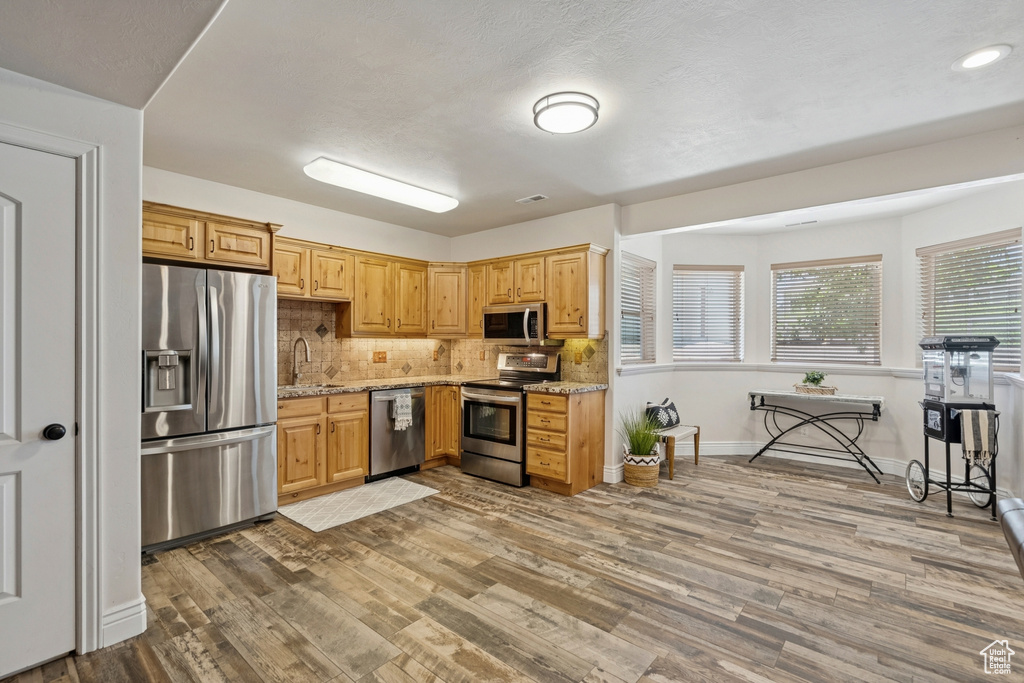 Kitchen with stainless steel appliances, wood finished floors, decorative backsplash, light stone counters, and recessed lighting
