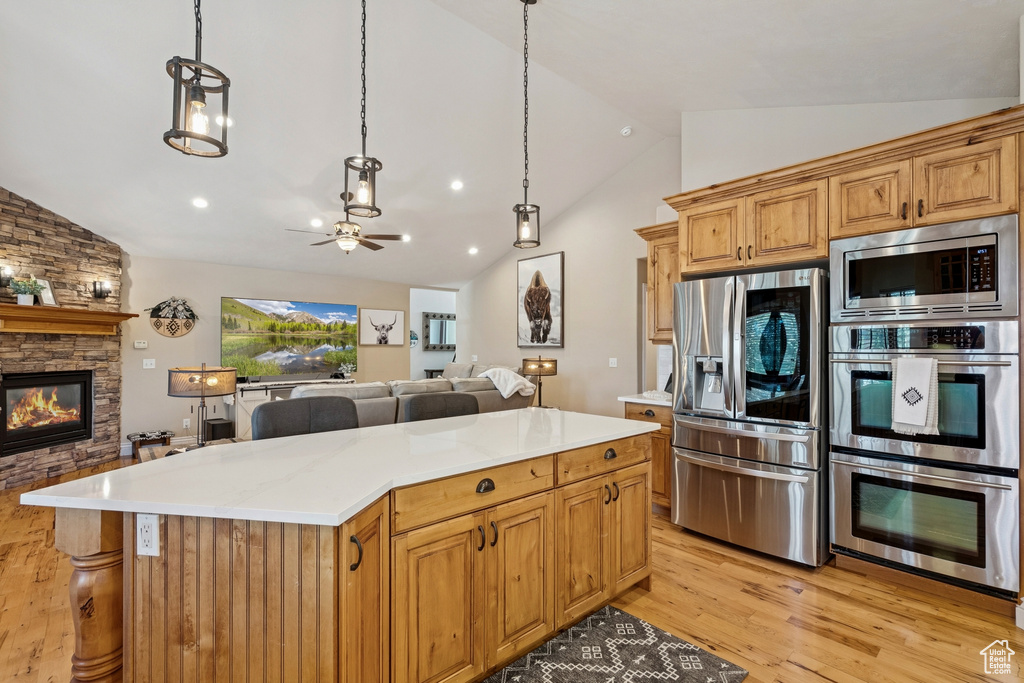Kitchen featuring appliances with stainless steel finishes, lofted ceiling, open floor plan, light wood-style floors, and a stone fireplace