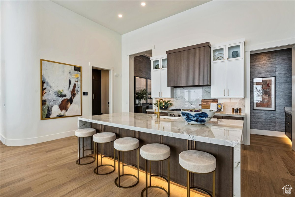 Kitchen with a breakfast bar, a kitchen island with sink, light wood-style floors, and recessed lighting