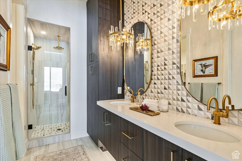 Full bathroom with a chandelier, a shower stall, double vanity, and backsplash