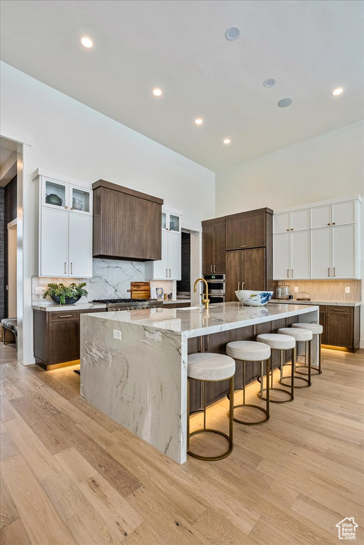 Kitchen featuring a breakfast bar, decorative backsplash, light wood finished floors, a spacious island, and glass insert cabinets