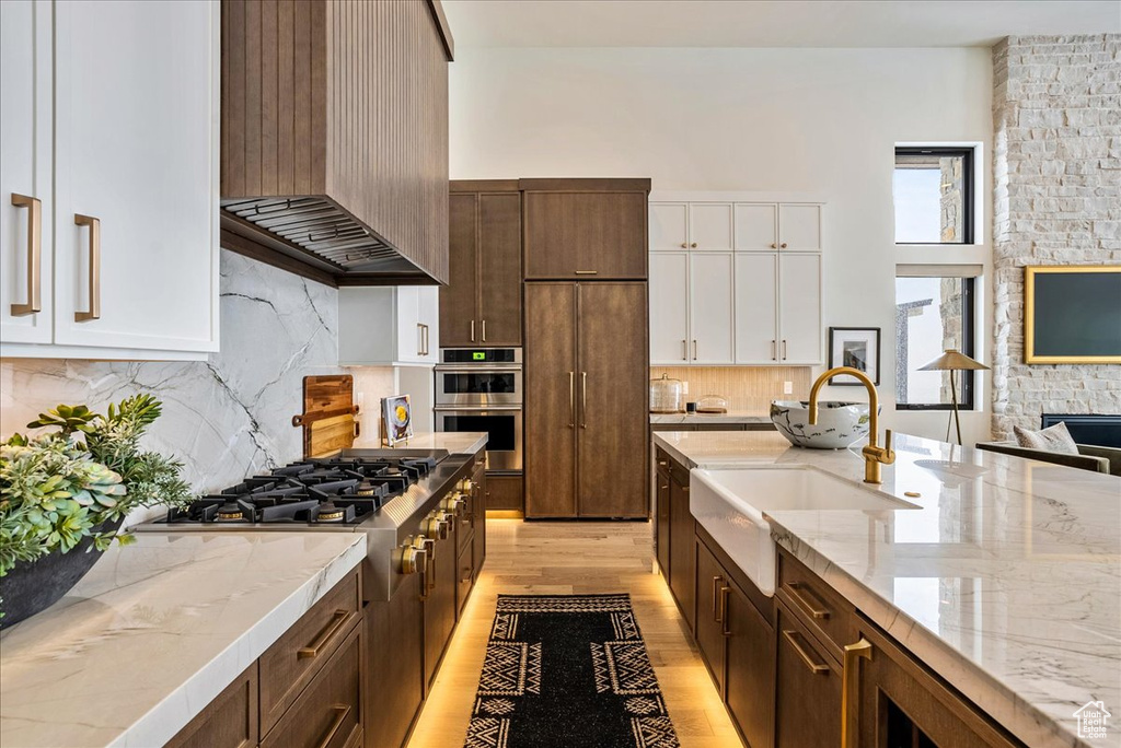 Kitchen featuring wall chimney exhaust hood, stainless steel appliances, white cabinets, light wood-type flooring, and decorative backsplash