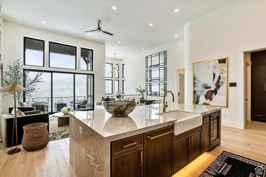 Kitchen featuring open floor plan, a ceiling fan, a towering ceiling, light wood-type flooring, and a center island with sink
