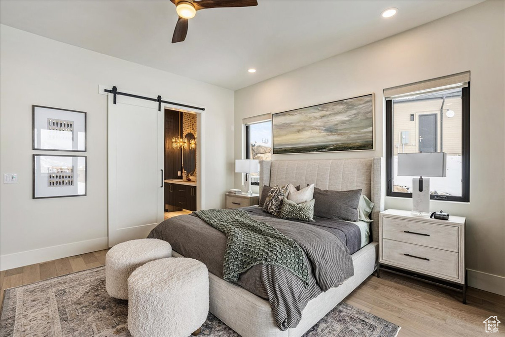 Bedroom featuring a barn door, wood finished floors, recessed lighting, ensuite bath, and a ceiling fan