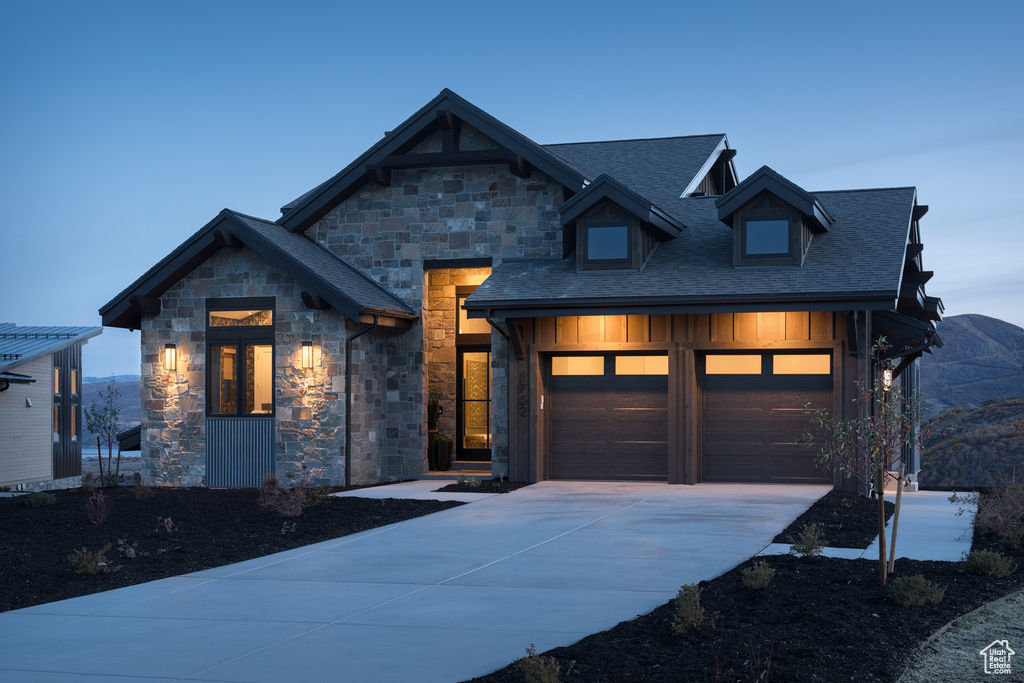 View of front of property with concrete driveway, stone siding, board and batten siding, an attached garage, and a shingled roof