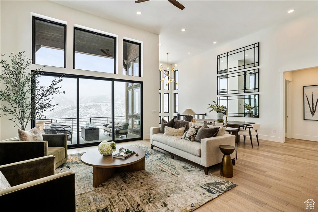 Living area with a towering ceiling, ceiling fan, light wood-style floors, recessed lighting, and a chandelier