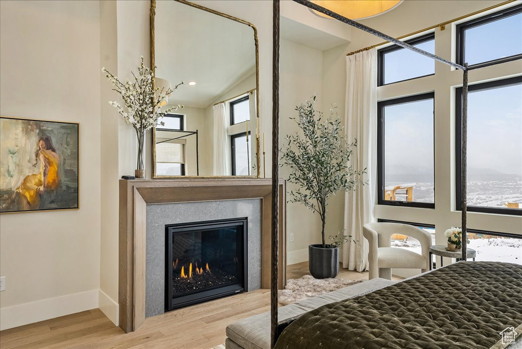 Bedroom featuring wood finished floors, a glass covered fireplace, and a towering ceiling