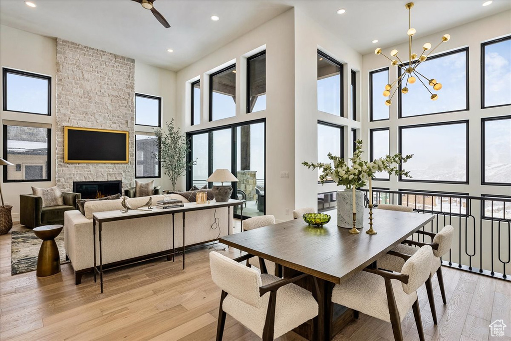 Dining space featuring light wood-style floors, recessed lighting, a ceiling fan, a high ceiling, and a stone fireplace