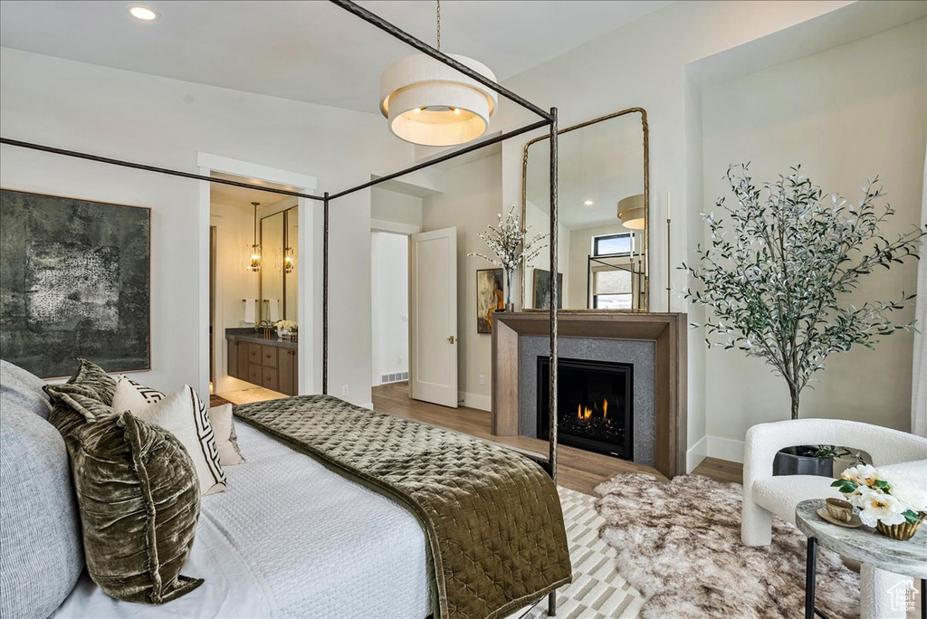 Bedroom with wood finished floors, a lit fireplace, and recessed lighting