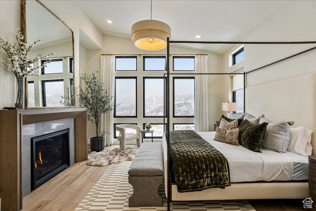 Bedroom with vaulted ceiling, wood finished floors, and a glass covered fireplace