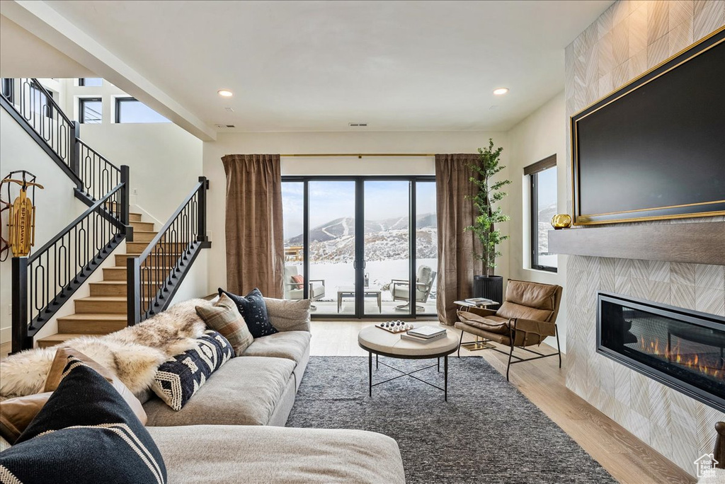 Living room with wood finished floors, a glass covered fireplace, stairs, and recessed lighting