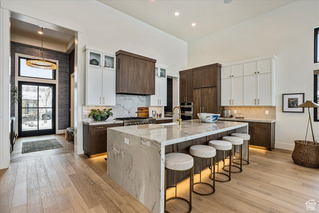 Kitchen with a towering ceiling, light wood-type flooring, a kitchen bar, a large island, and light stone counters
