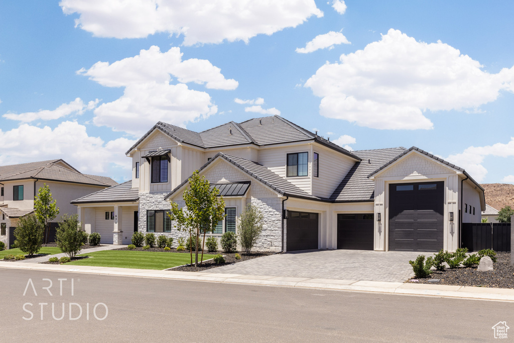 View of front of home featuring a garage, stone siding, decorative driveway, a tiled roof, and board and batten siding