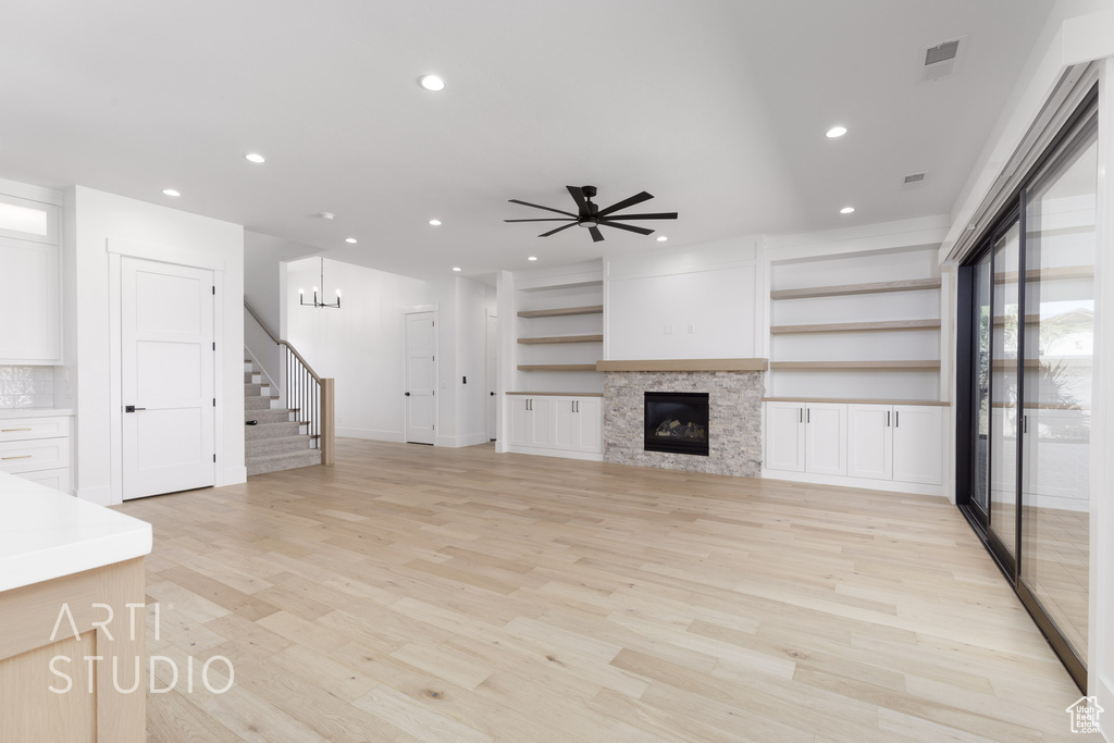 Unfurnished living room with stairs, recessed lighting, light wood finished floors, a ceiling fan, and a glass covered fireplace