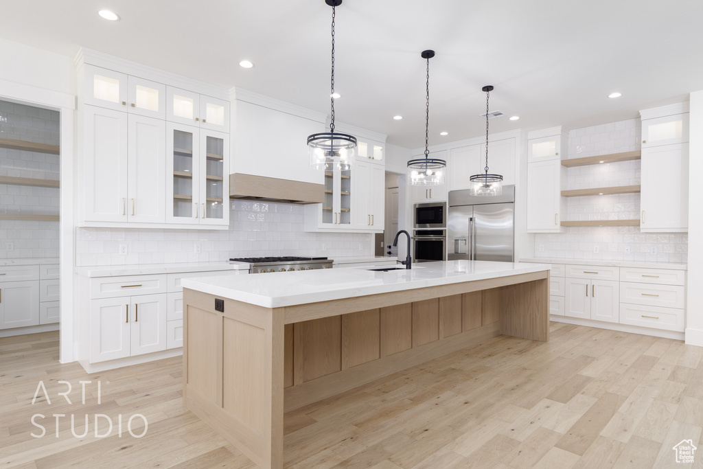 Kitchen featuring built in appliances, open shelves, backsplash, light countertops, and a large island with sink