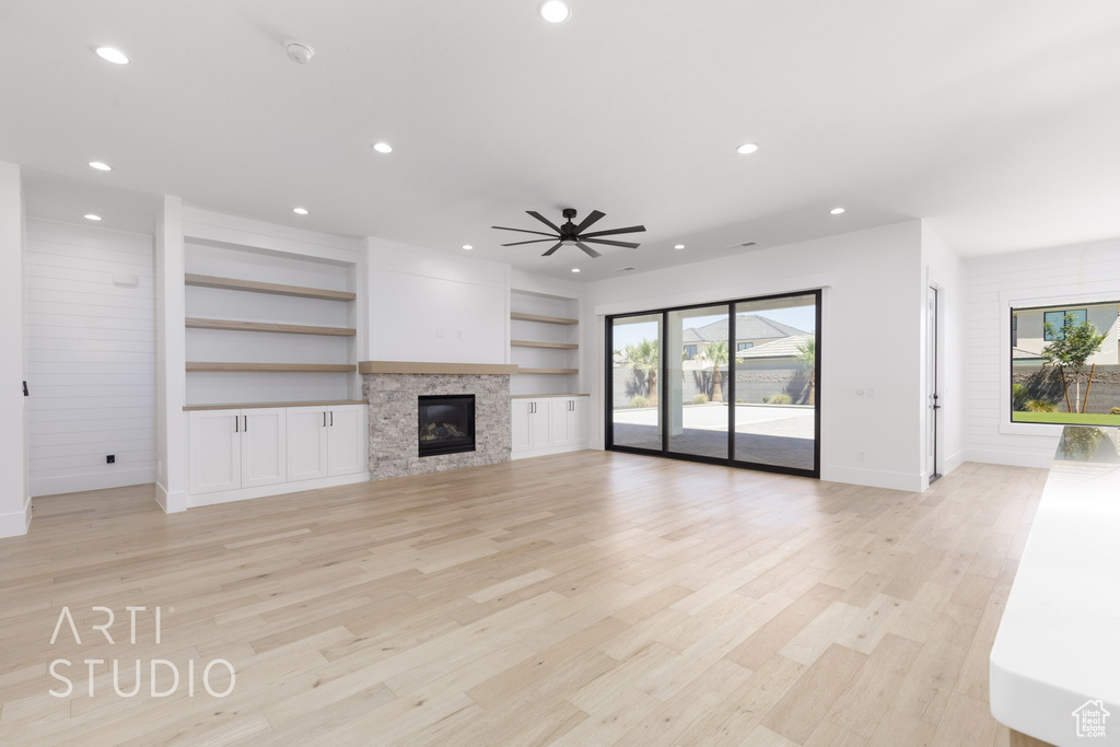 Unfurnished living room with recessed lighting, light wood-style flooring, ceiling fan, built in features, and a glass covered fireplace