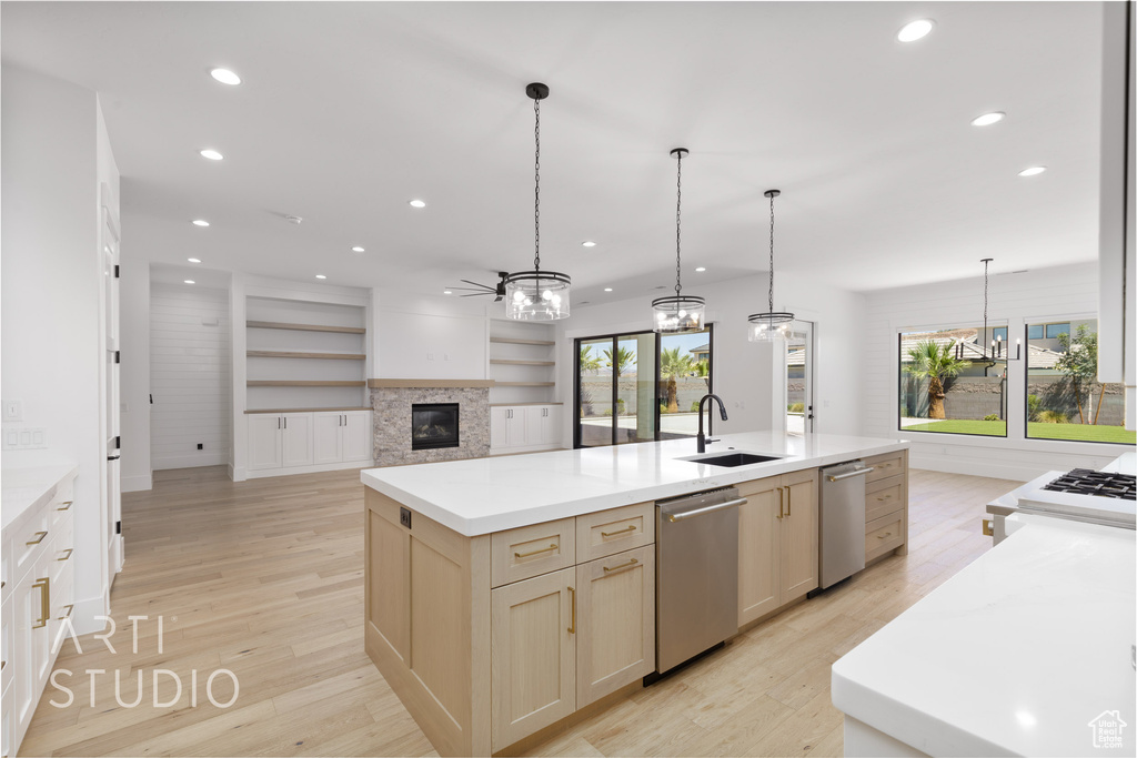 Kitchen with stainless steel dishwasher, a glass covered fireplace, a kitchen island with sink, recessed lighting, and light wood-style flooring