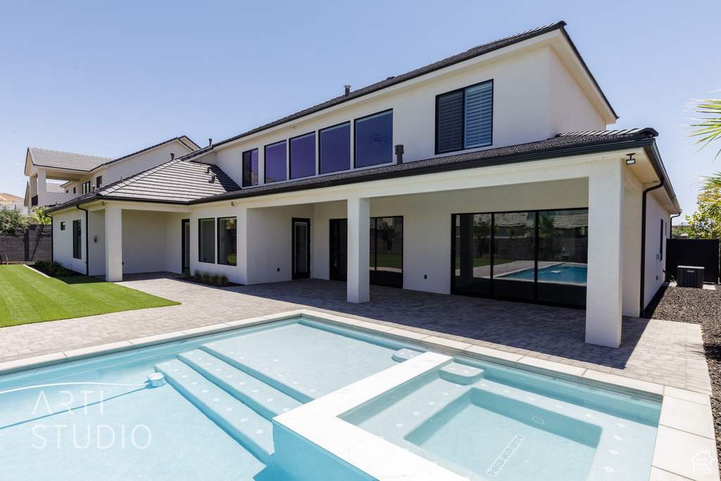Back of house with stucco siding, a pool with connected hot tub, and a patio