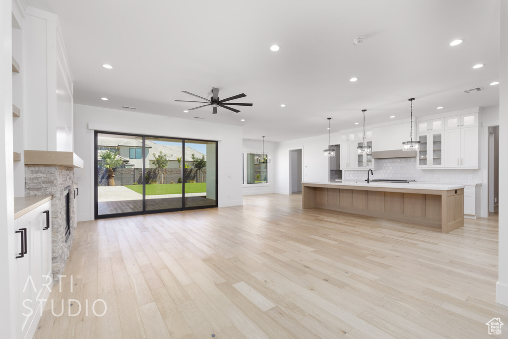 Kitchen featuring open floor plan, decorative backsplash, a ceiling fan, a fireplace, and light countertops