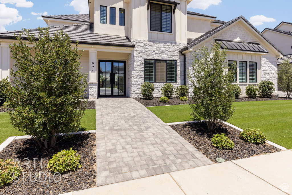 Modern farmhouse featuring stone siding, french doors, a front lawn, and board and batten siding