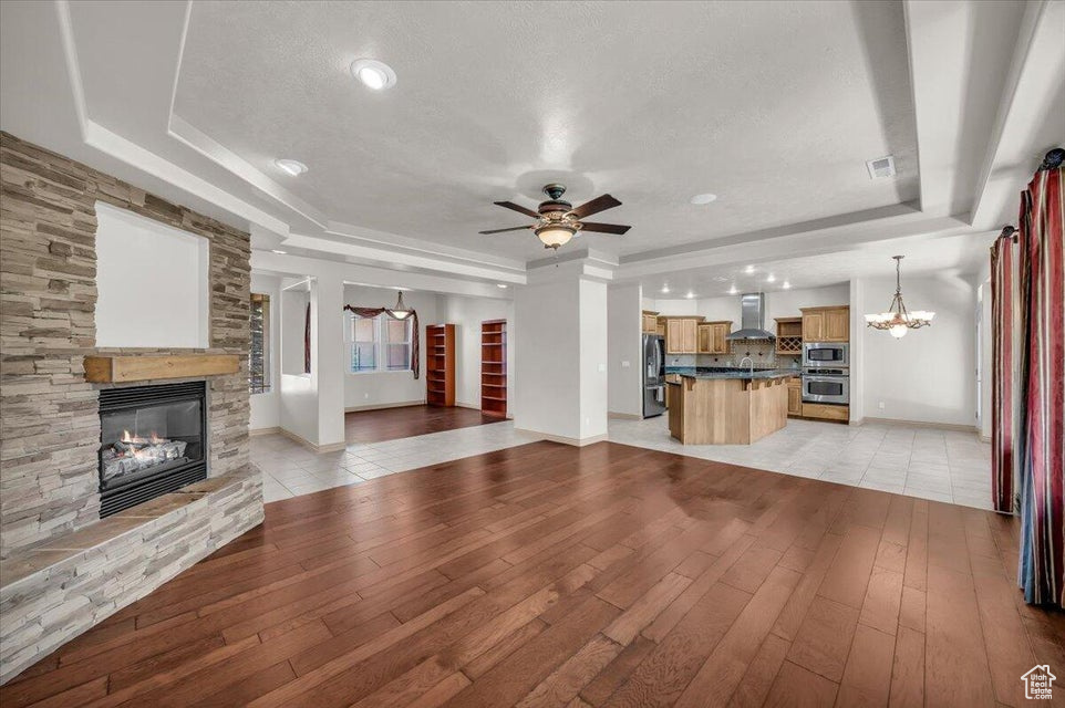 Unfurnished living room featuring a raised ceiling, a fireplace, a chandelier, light wood-style flooring, and a textured ceiling