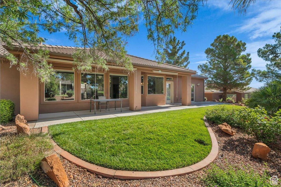 Rear view of property with stucco siding, a patio area, a tile roof, and a lawn