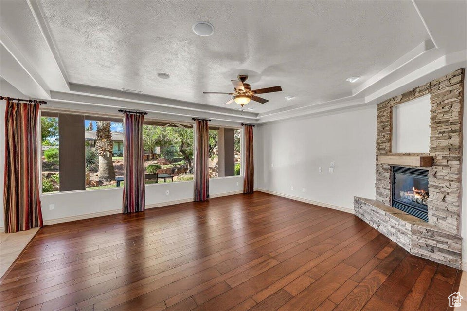 Unfurnished living room featuring a raised ceiling, a fireplace, a ceiling fan, and a textured ceiling