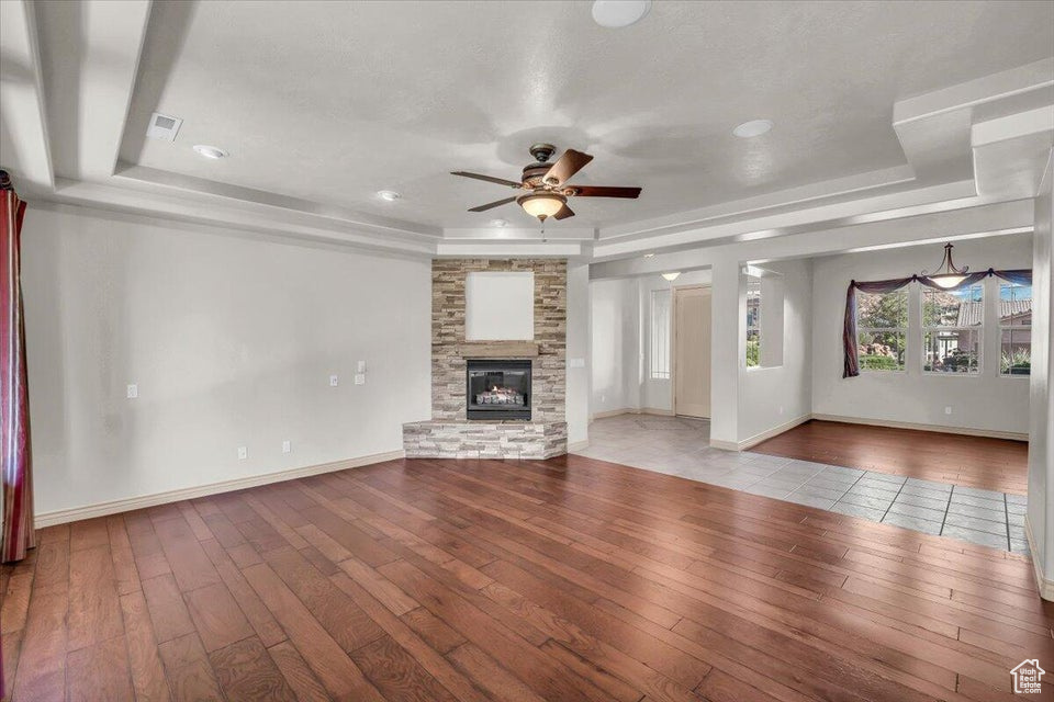 Unfurnished living room with hardwood / wood-style floors, a raised ceiling, ceiling fan, a fireplace, and recessed lighting