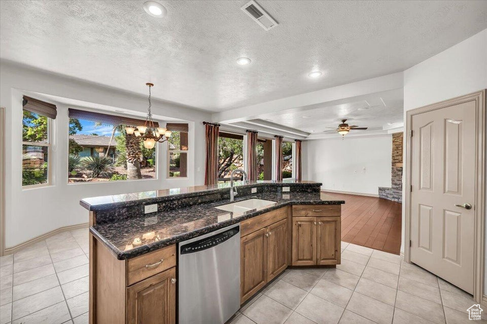 Kitchen with stainless steel dishwasher, a chandelier, light tile patterned floors, brown cabinetry, and a textured ceiling