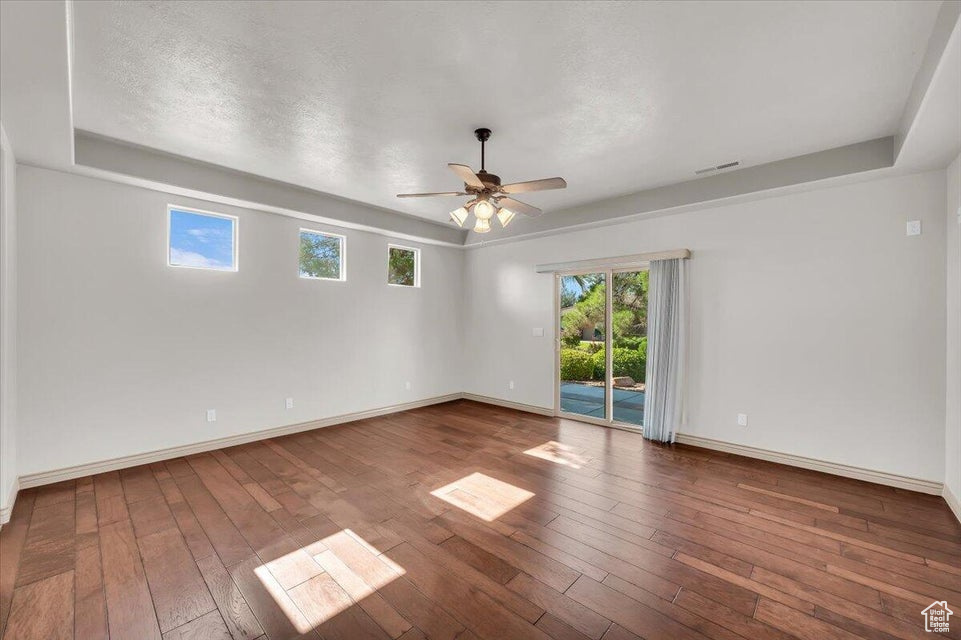 Empty room featuring ceiling fan, hardwood / wood-style flooring, a raised ceiling, and a textured ceiling