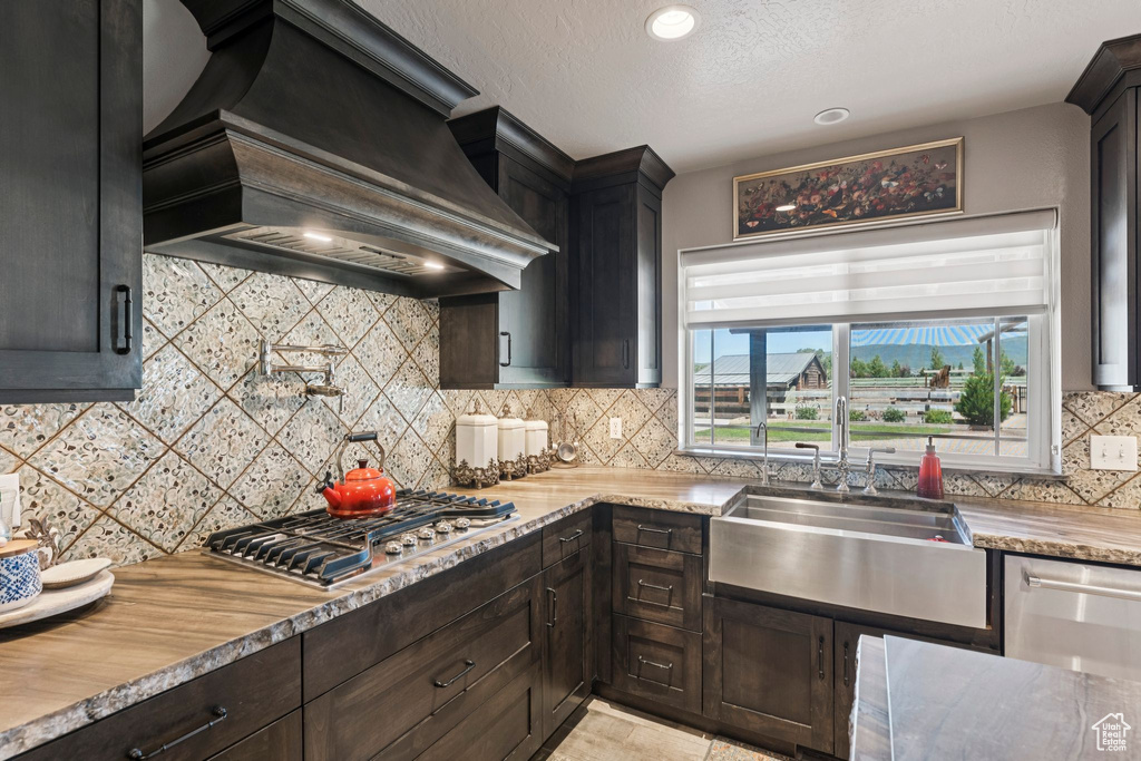 Kitchen featuring custom exhaust hood, stainless steel gas stovetop, tasteful backsplash, a textured ceiling, and recessed lighting