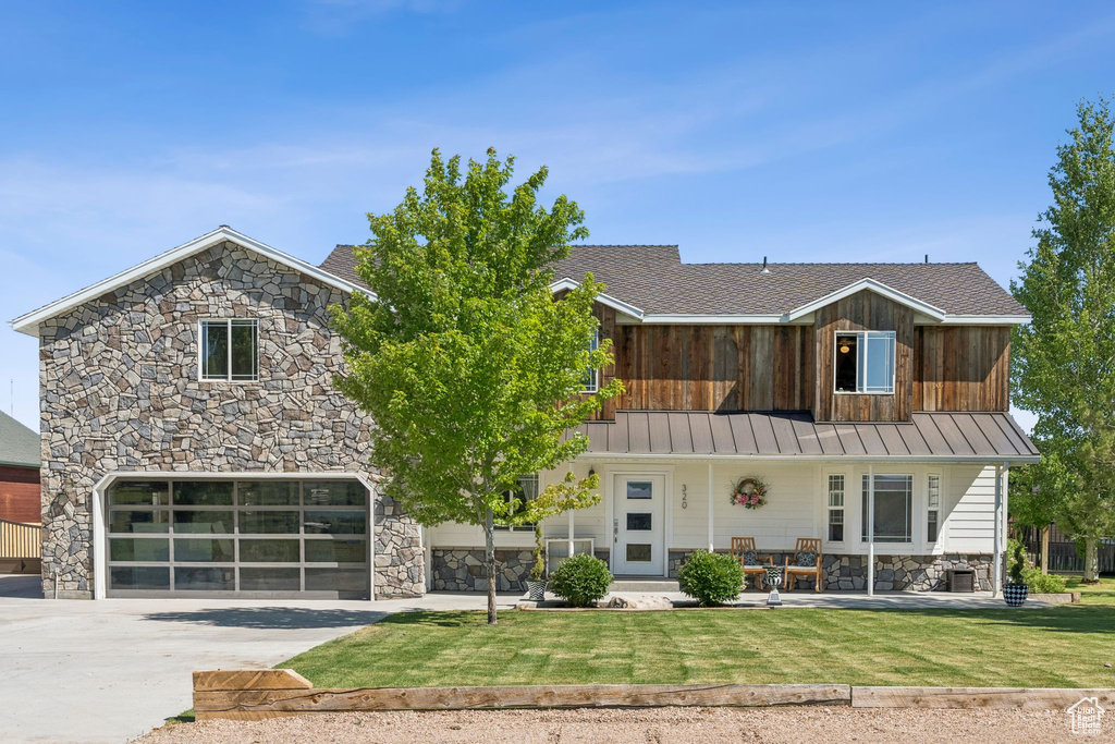 View of front of home featuring stone siding, an attached garage, a standing seam roof, concrete driveway, and a front yard