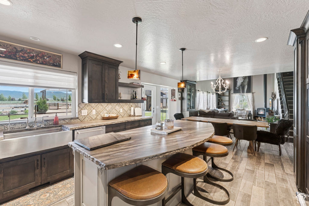 Kitchen featuring dark brown cabinets, plenty of natural light, a chandelier, a center island, and a textured ceiling