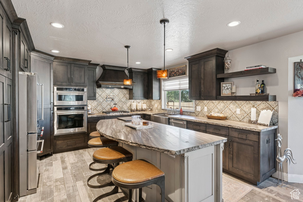 Kitchen featuring premium range hood, stainless steel appliances, a kitchen island, light wood-style flooring, and a textured ceiling