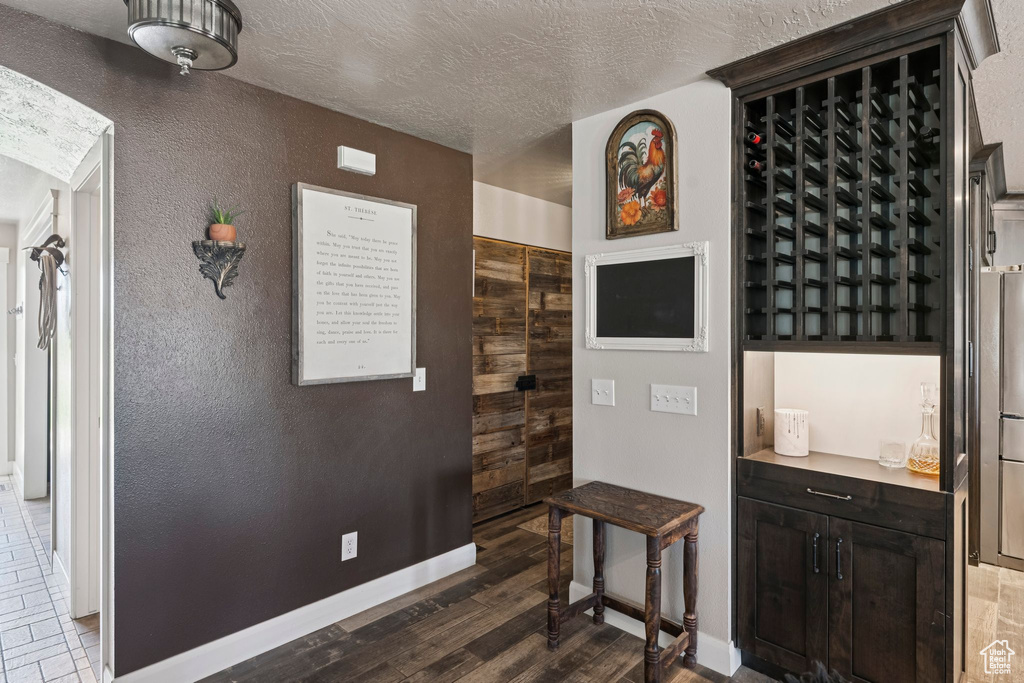 Wine room with dark wood-style floors, a textured ceiling, and a textured wall