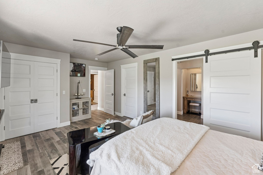 Bedroom featuring a barn door, dark wood finished floors, a ceiling fan, and ensuite bathroom