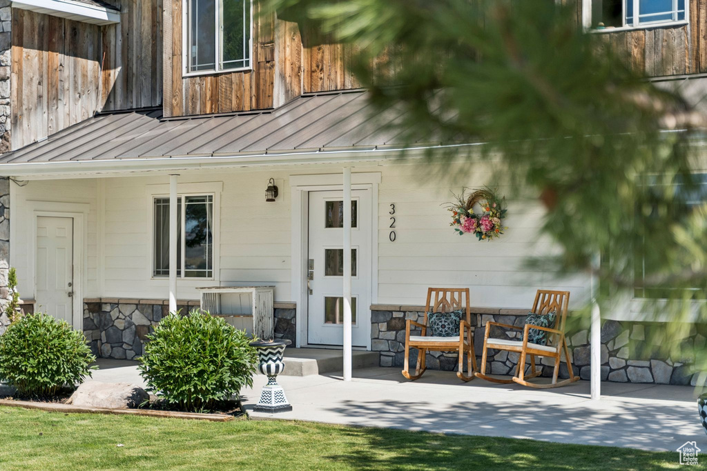 Back of house with a standing seam roof, stone siding, a patio, and a metal roof