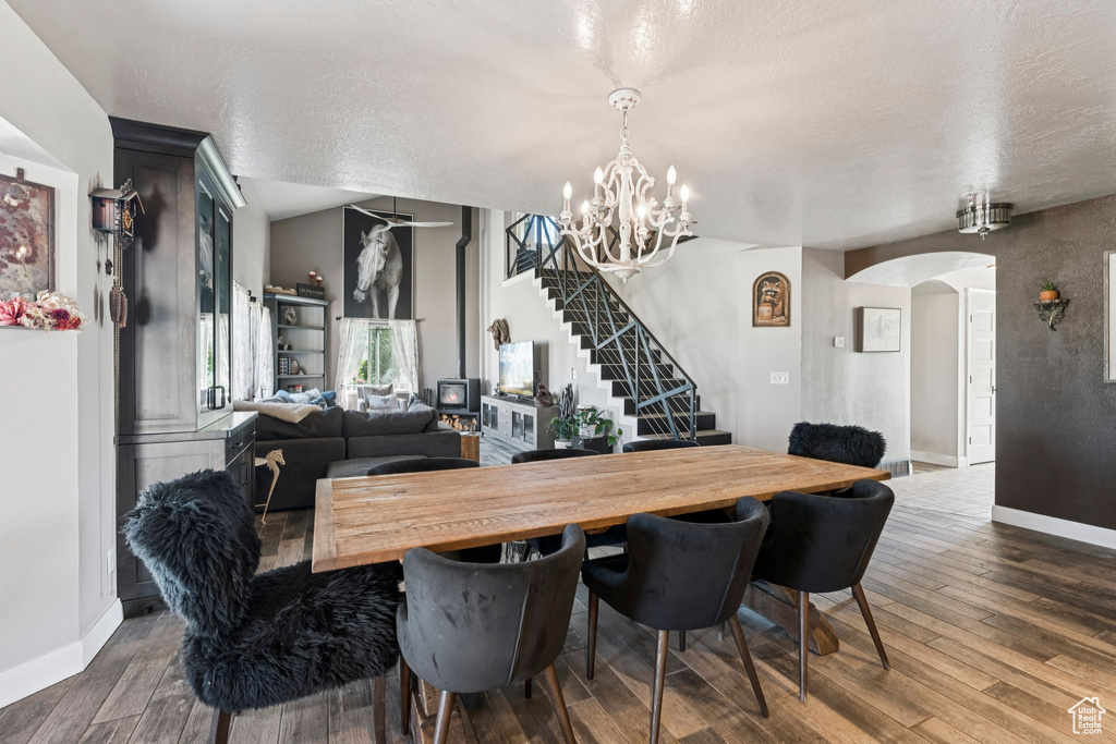 Dining space with arched walkways, stairway, dark wood-style flooring, a chandelier, and a textured ceiling