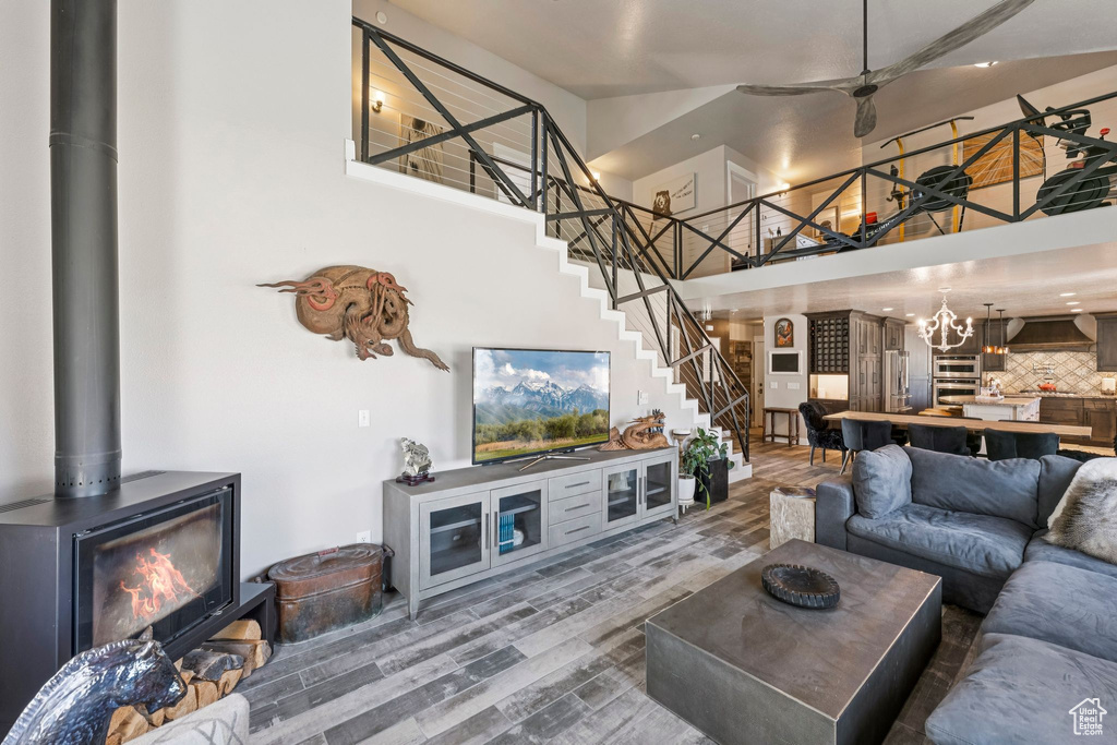 Living room with a high ceiling, stairs, wood finished floors, a wood stove, and ceiling fan