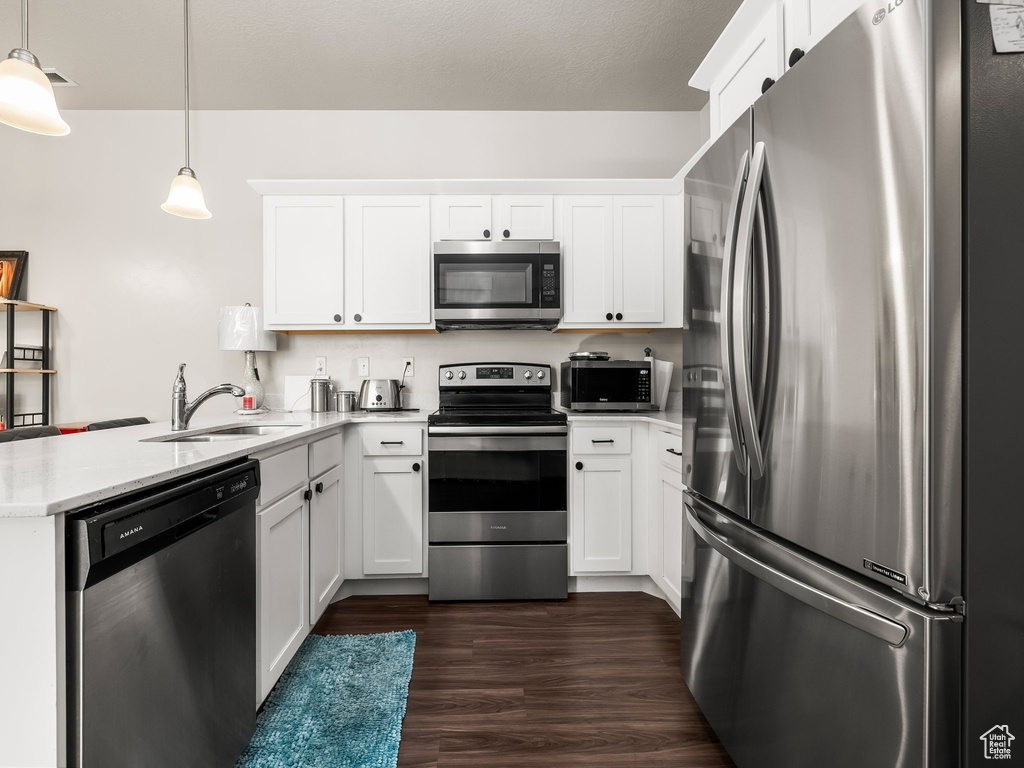 Kitchen featuring appliances with stainless steel finishes, a peninsula, white cabinets, and decorative light fixtures