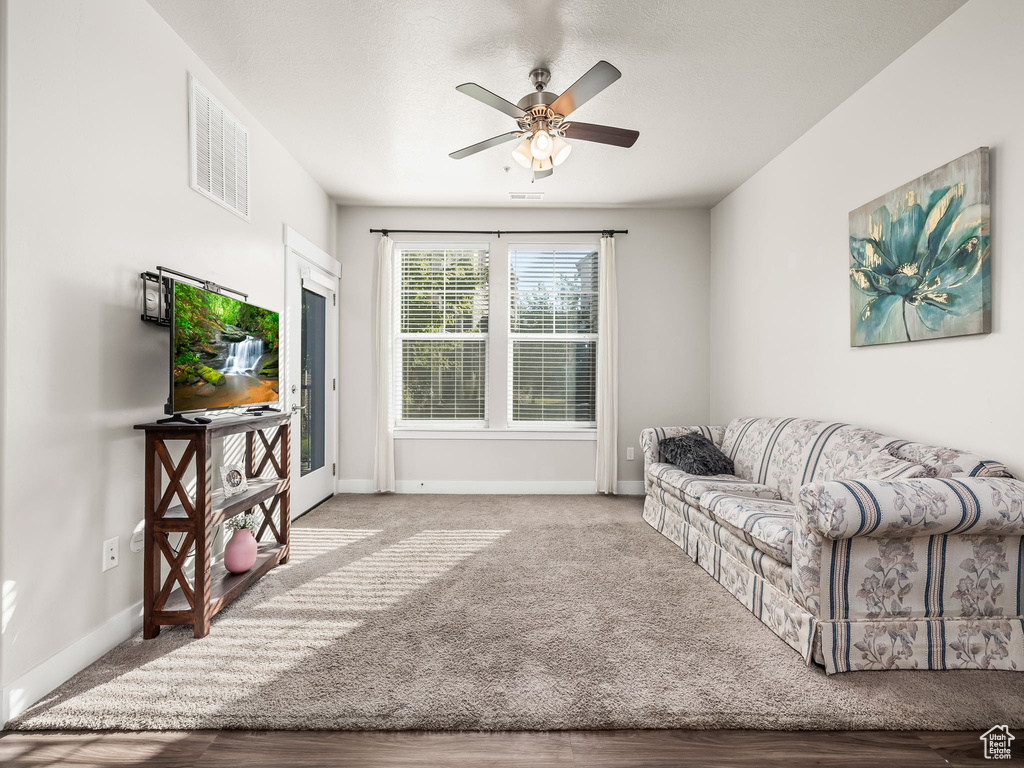 Carpeted living area with a ceiling fan and baseboards