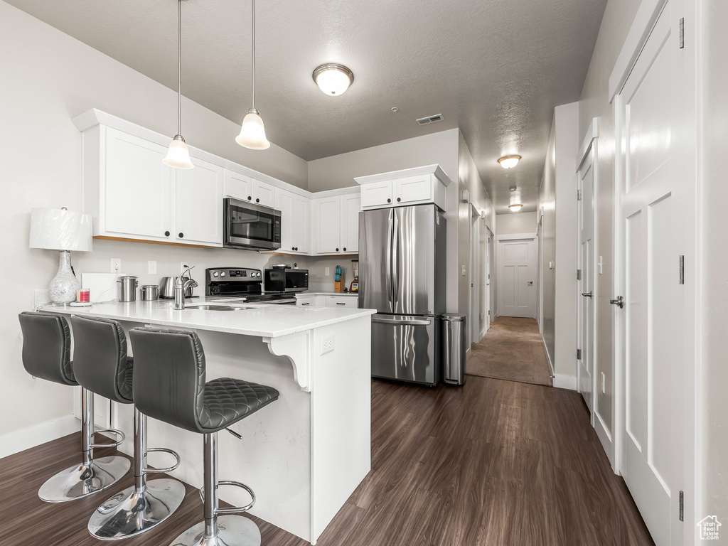 Kitchen with stainless steel appliances, a peninsula, dark wood finished floors, light countertops, and a kitchen breakfast bar
