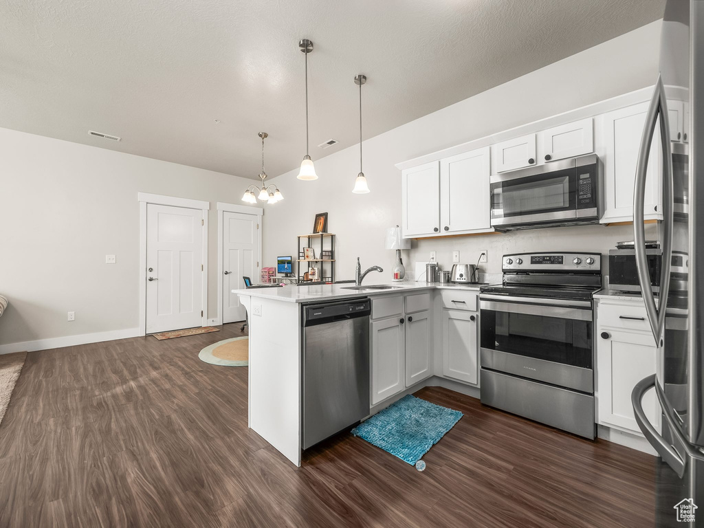 Kitchen featuring appliances with stainless steel finishes, a peninsula, dark wood-type flooring, a chandelier, and white cabinetry