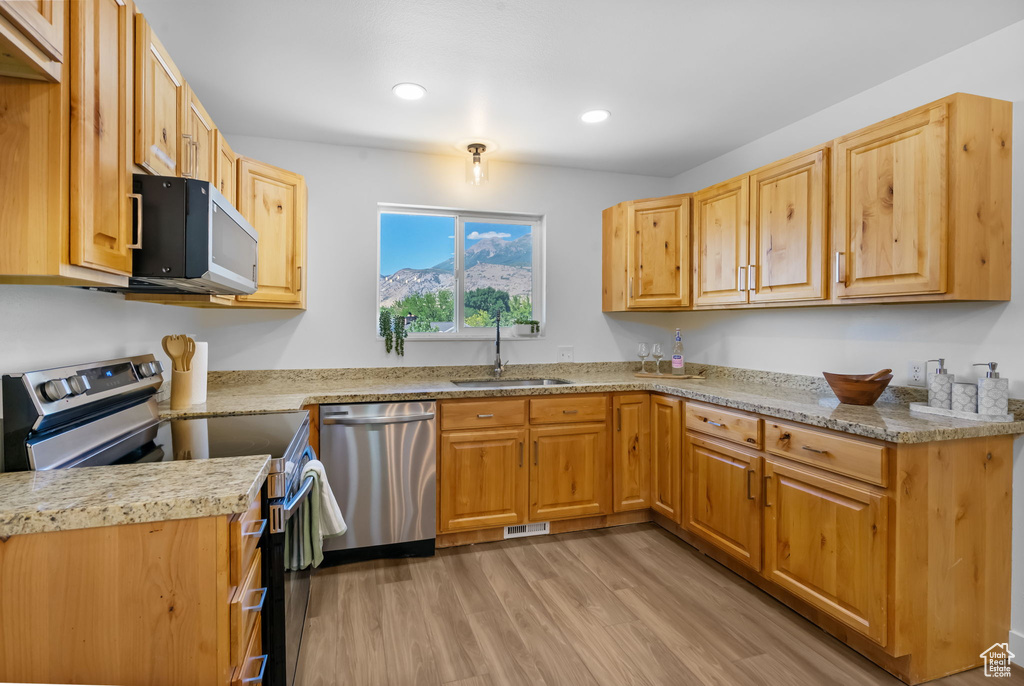 Kitchen with appliances with stainless steel finishes, light wood-type flooring, recessed lighting, and light stone countertops