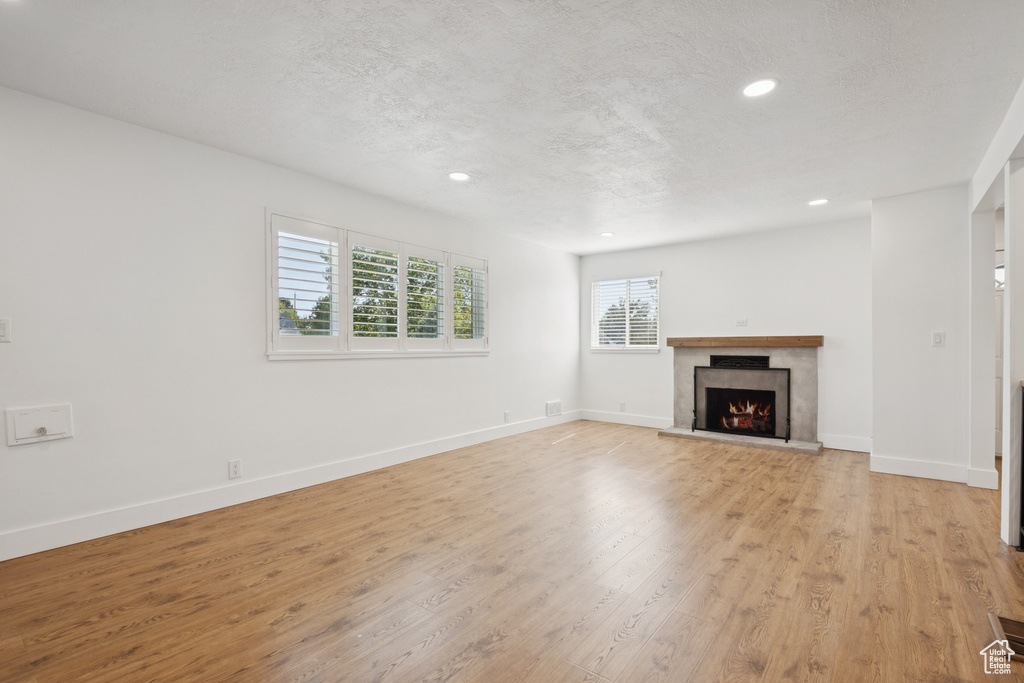 Unfurnished living room with recessed lighting, a premium fireplace, light wood finished floors, and a textured ceiling